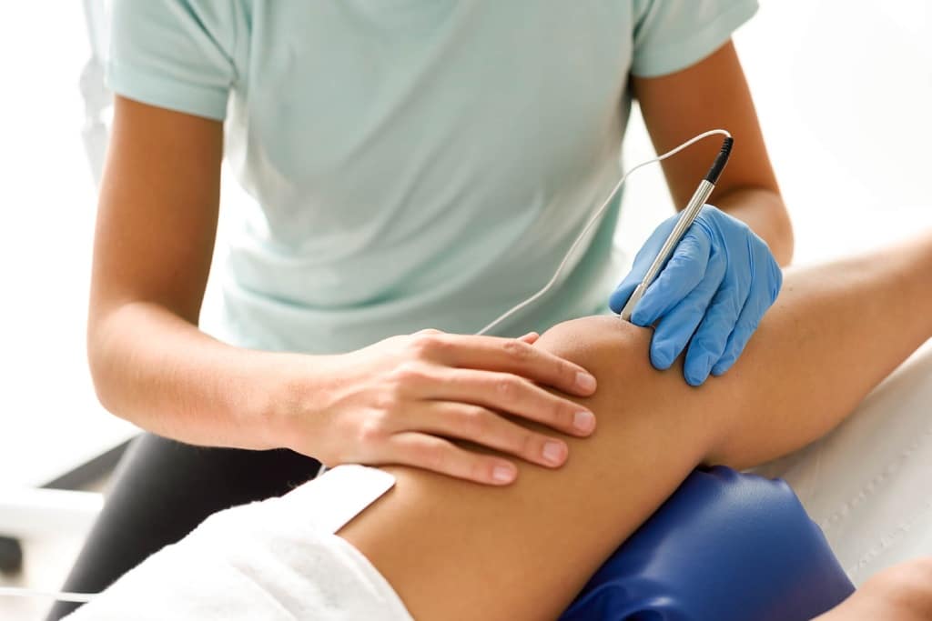 fisio aplicando tratamiento en la rodilla de la paciente min